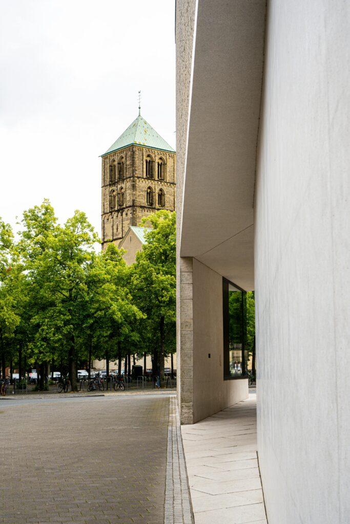 Bell tower amidst urban architecture in Münster, Germany, featuring Gothic and Romanesque styles.